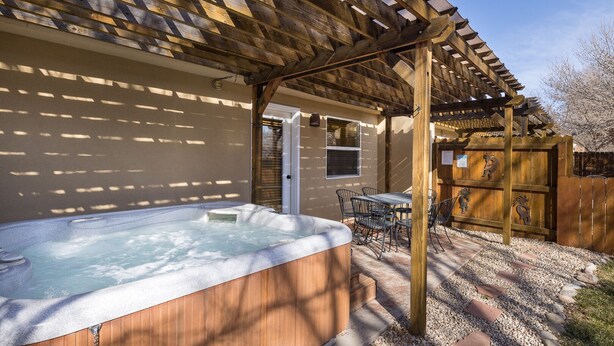 A hot tub under a wooden pergola with a patio table and chairs, surrounded by a wooden fence and a gravel path. - Cottonwoods 419 (Moab)