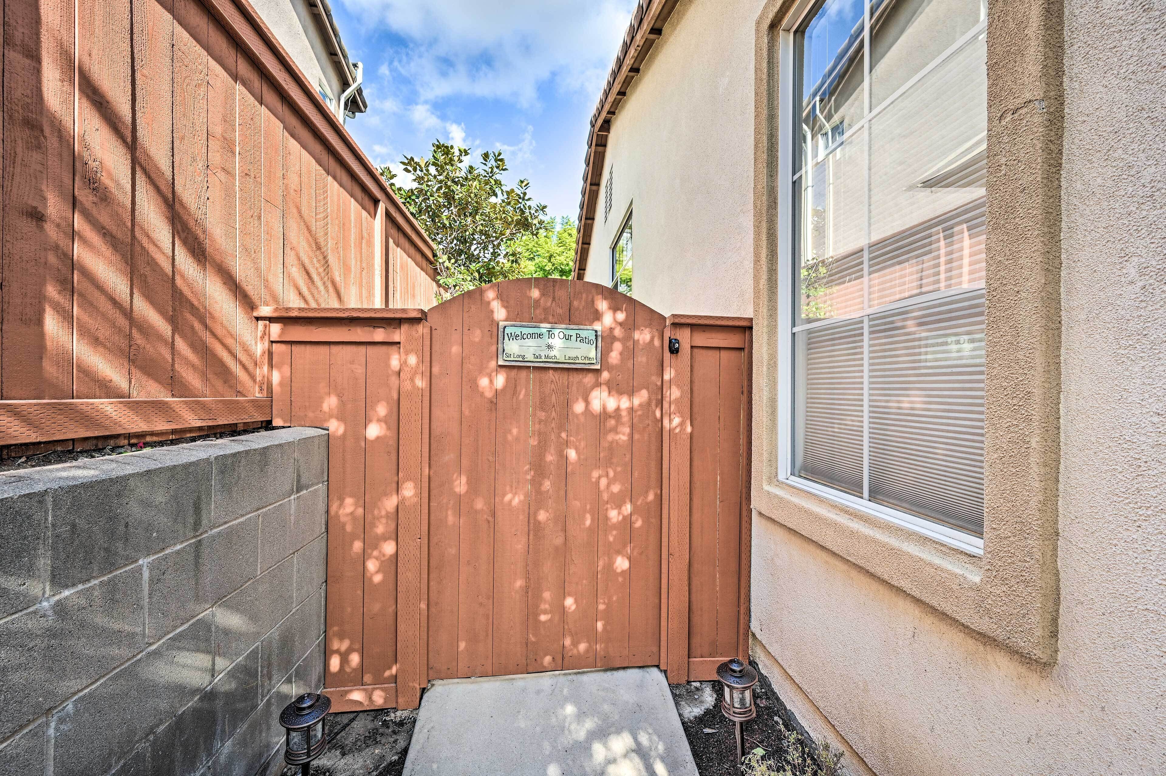 Une porte en bois avec une pancarte indiquant l’entrée d’un espace patio, une marche en béton menant à la porte, et une petite lanterne posée sur le sol.