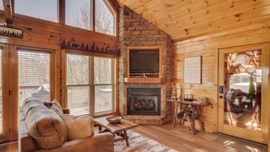 Un intérieur de chalet chaleureux avec une cheminée en pierre, des murs en bois et de grandes fenêtres.