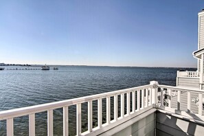 A waterfront view from a balcony with a railing, a dock in the distance, and a clear sky.