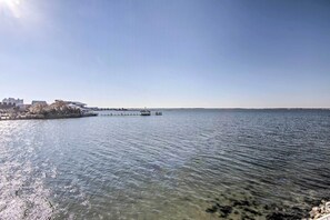 A waterfront view with a pier extending into the water, buildings on the shore, and clear skies.