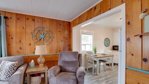 A cozy living room with a grey armchair, a patterned throw pillow, a small table with a lamp, and a wooden wall with a compass decoration. - Oceanview Rockaway Beach Condo w/ Deck & Gas Grill (Rockaway Beach)