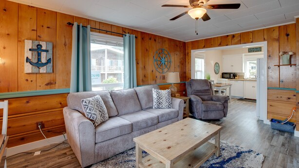 A cozy living room with a wooden ceiling, a ceiling fan, a gray sofa with patterned cushions, a wooden coffee table, and a view into the kitchen through an open doorway. - Oceanview Rockaway Beach Condo w/ Deck & Gas Grill (Rockaway Beach)