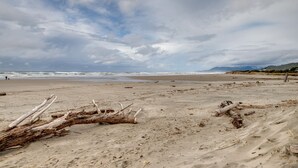 A beach with driftwood and a person walking in the distance. - Oceanview Rockaway Beach Condo w/ Deck & Gas Grill (Rockaway Beach)