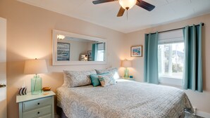 A bedroom with a bed, nightstands, a ceiling fan, a window with curtains, and a wall-mounted mirror. - Oceanview Rockaway Beach Condo w/ Deck & Gas Grill (Rockaway Beach)