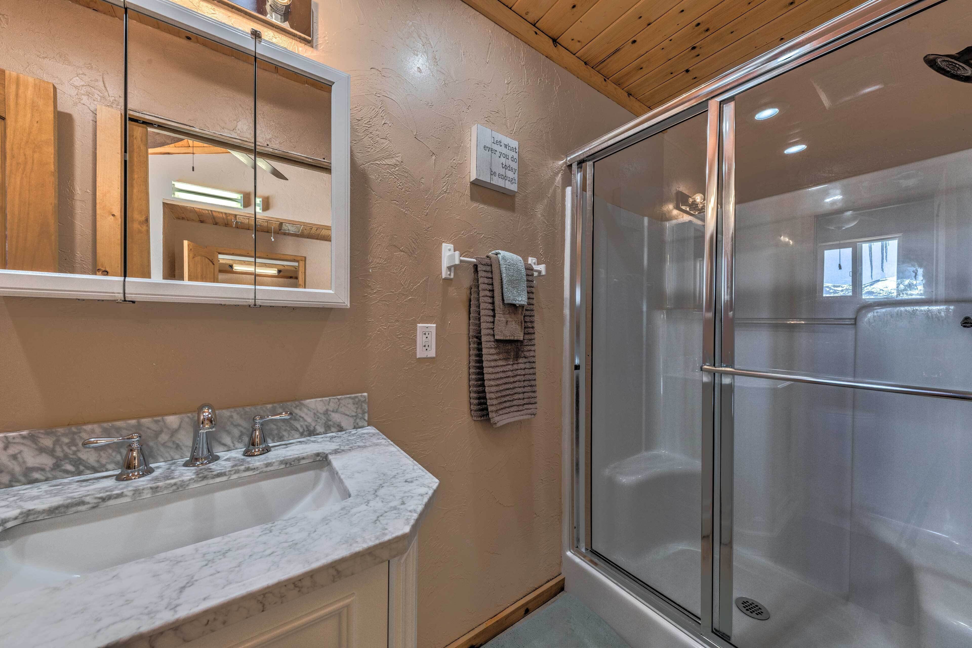 A bathroom with a marble sink, a glass-enclosed shower, and a mirror with a motivational quote.