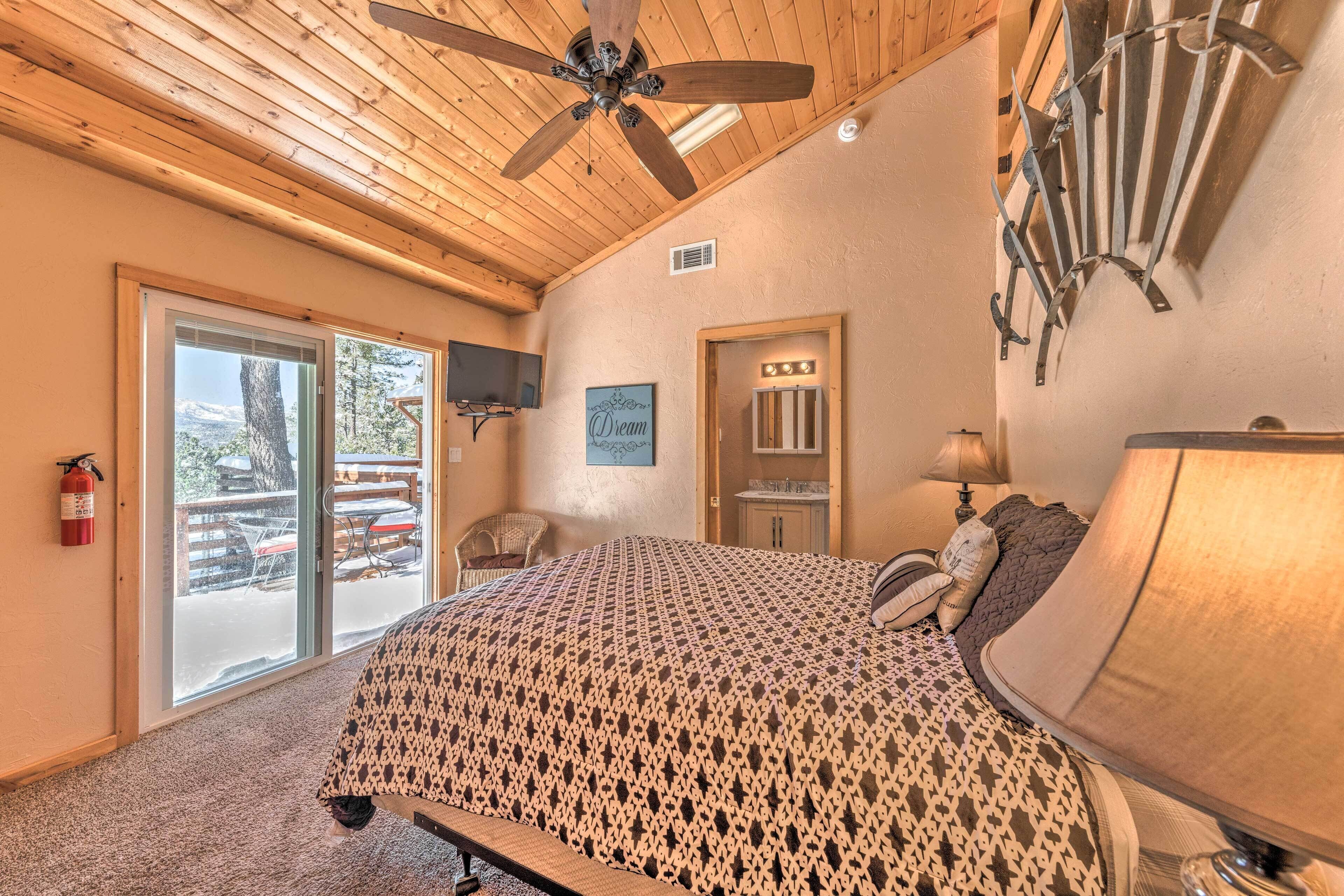 A bedroom with a bed, a ceiling fan, a TV, a mirror, and a window with a view of the outdoors.