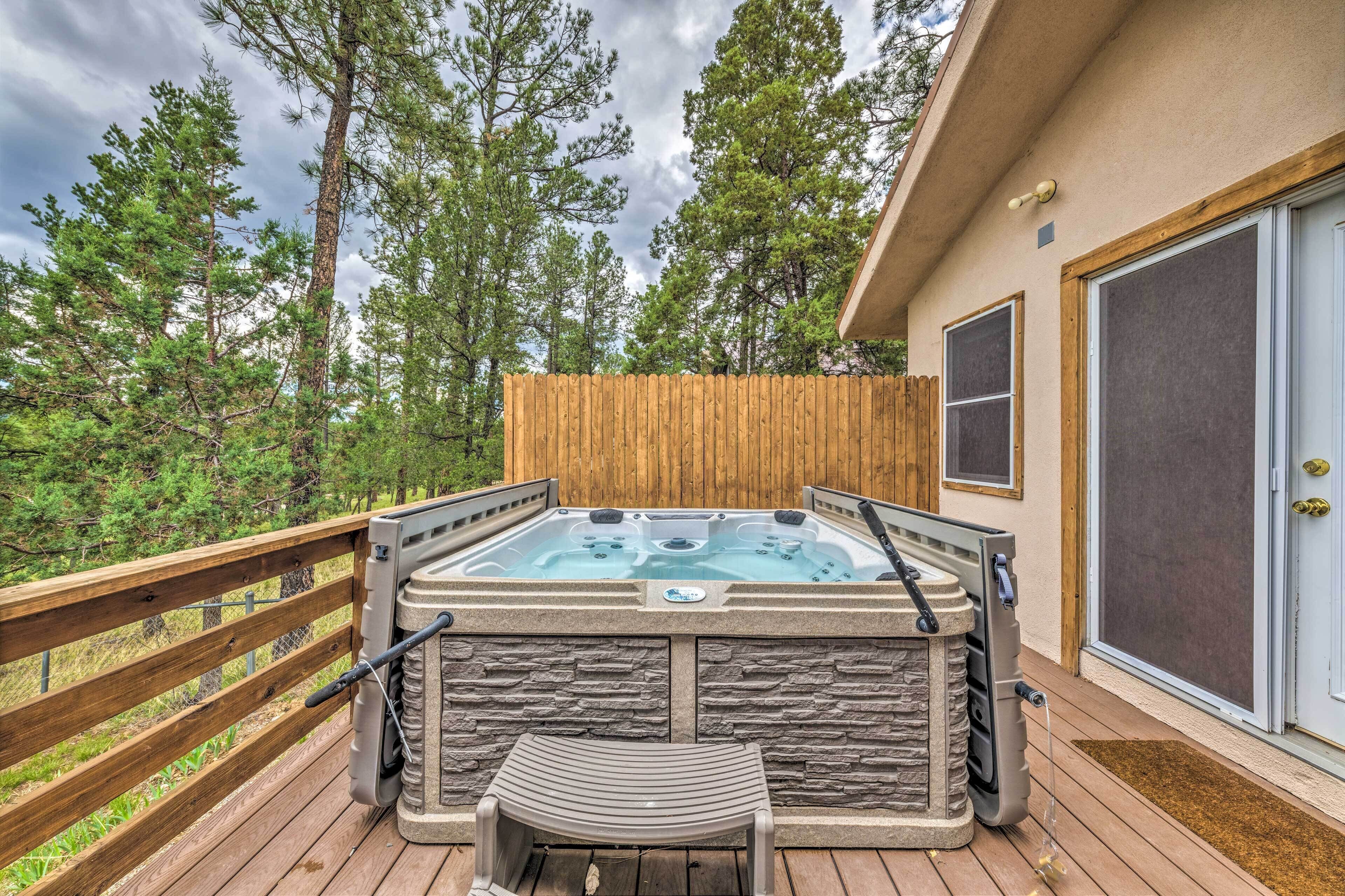 A hot tub on a wooden deck with a stone wall, a wooden fence, and a door with a screen.