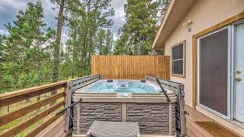 A hot tub on a wooden deck with a stone wall, a wooden fence, and a door with a screen.