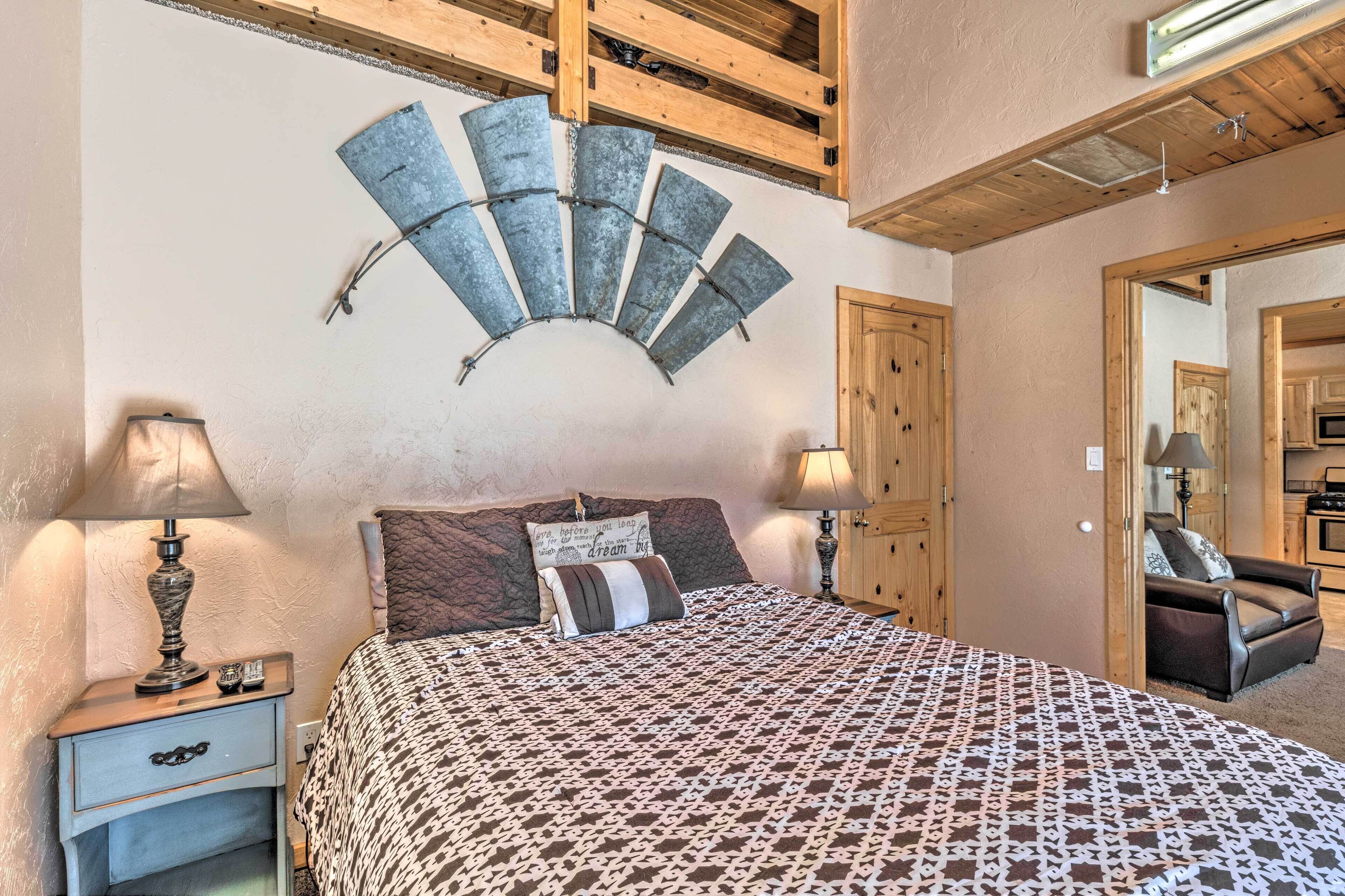 Un dormitorio con una cama, dos mesitas de noche, un ventilador de pared y techo de madera.