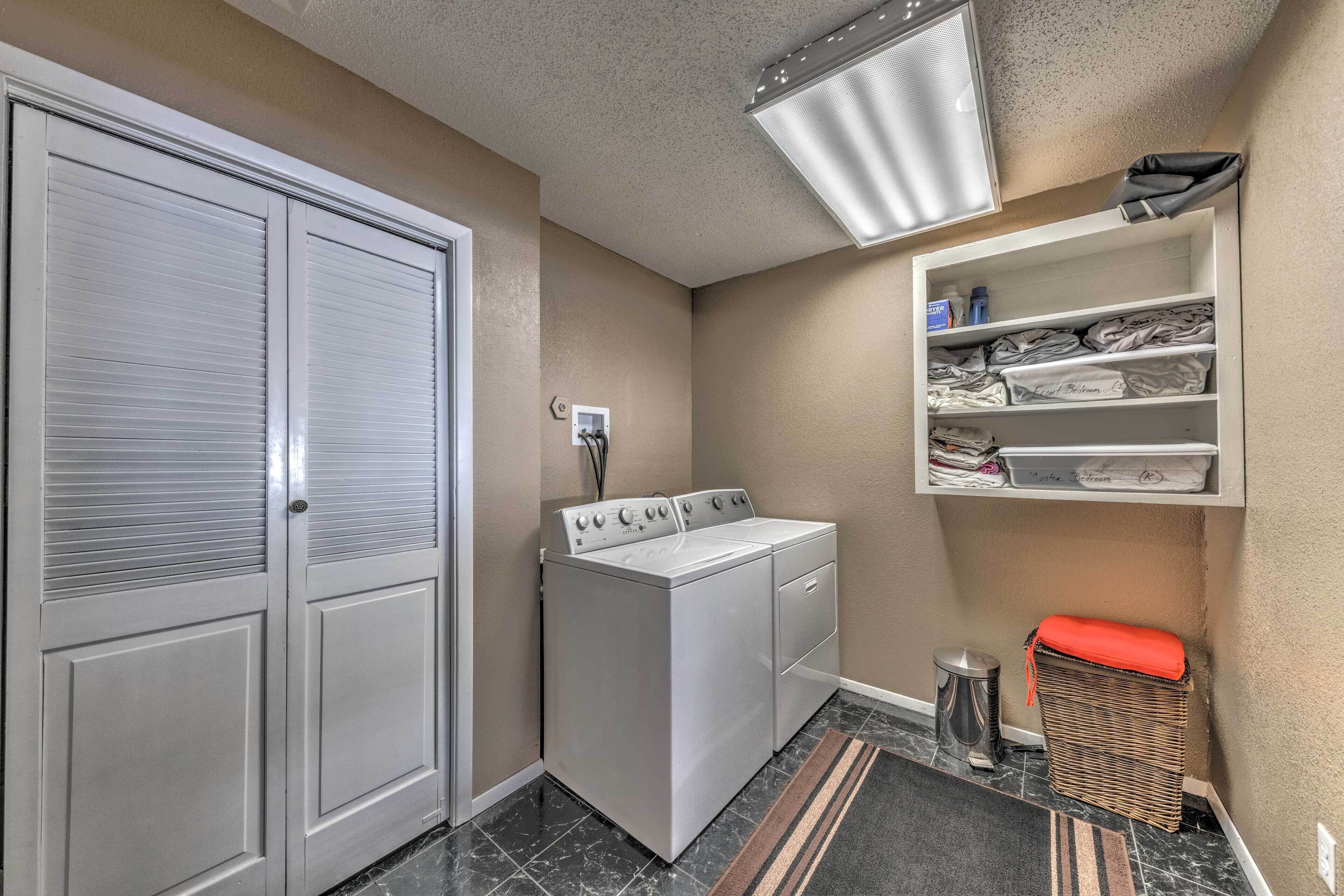 A laundry room with a washer and dryer, a shelf with folded clothes, and a trash can.