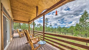 Terraza de madera con mecedoras y una pequeña mesa, con vistas a un área boscosa.