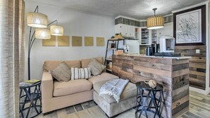 A modern living room with a sofa, a coffee table, and a wooden island with bar stools. - Steps to Sand + 2 Pools! Galveston Coastal Getaway (Galveston)