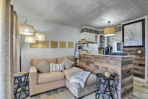 Uma sala de estar moderna com sofá, mesa de centro e uma ilha de madeira com banquetas.