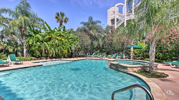 A clear swimming pool with lounge chairs and palm trees. - Steps to Sand + 2 Pools! Galveston Coastal Getaway (Galveston)