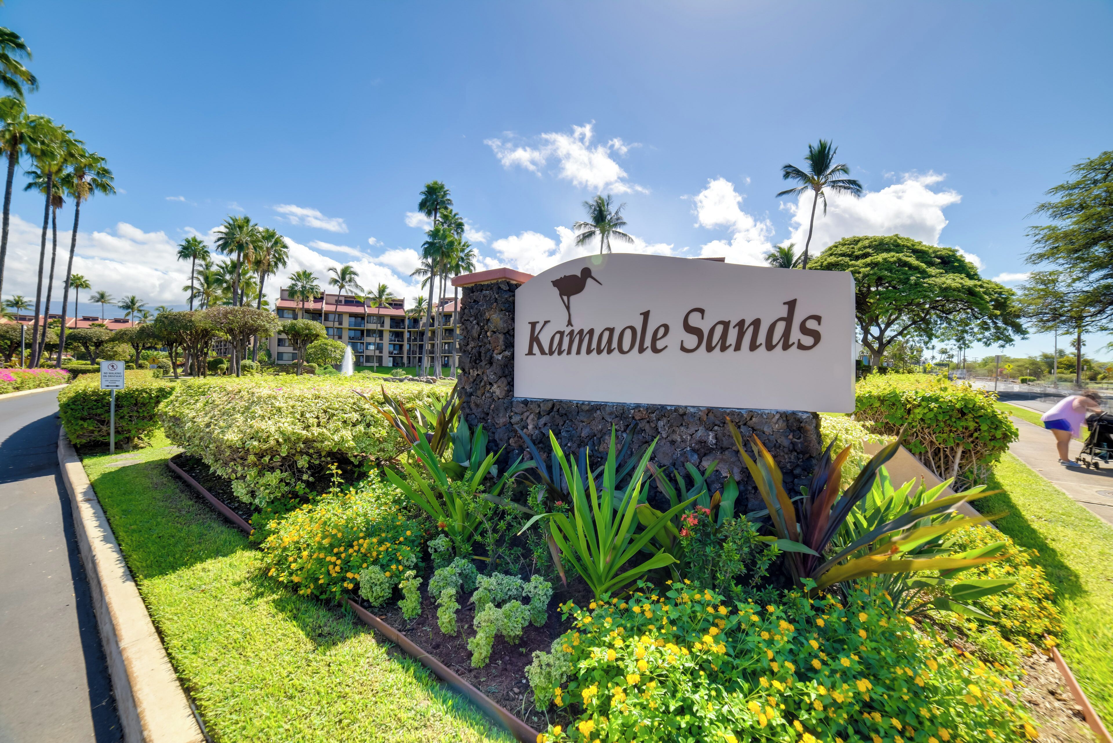 Señal de Kamaole Sands con silueta de ave, rodeada de jardines cuidados y palmeras.