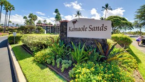 Naamplaatje voor Kamaole Sands, met een silhouet van een vogel, omgeven door verzorgde tuinen en palmbomen.