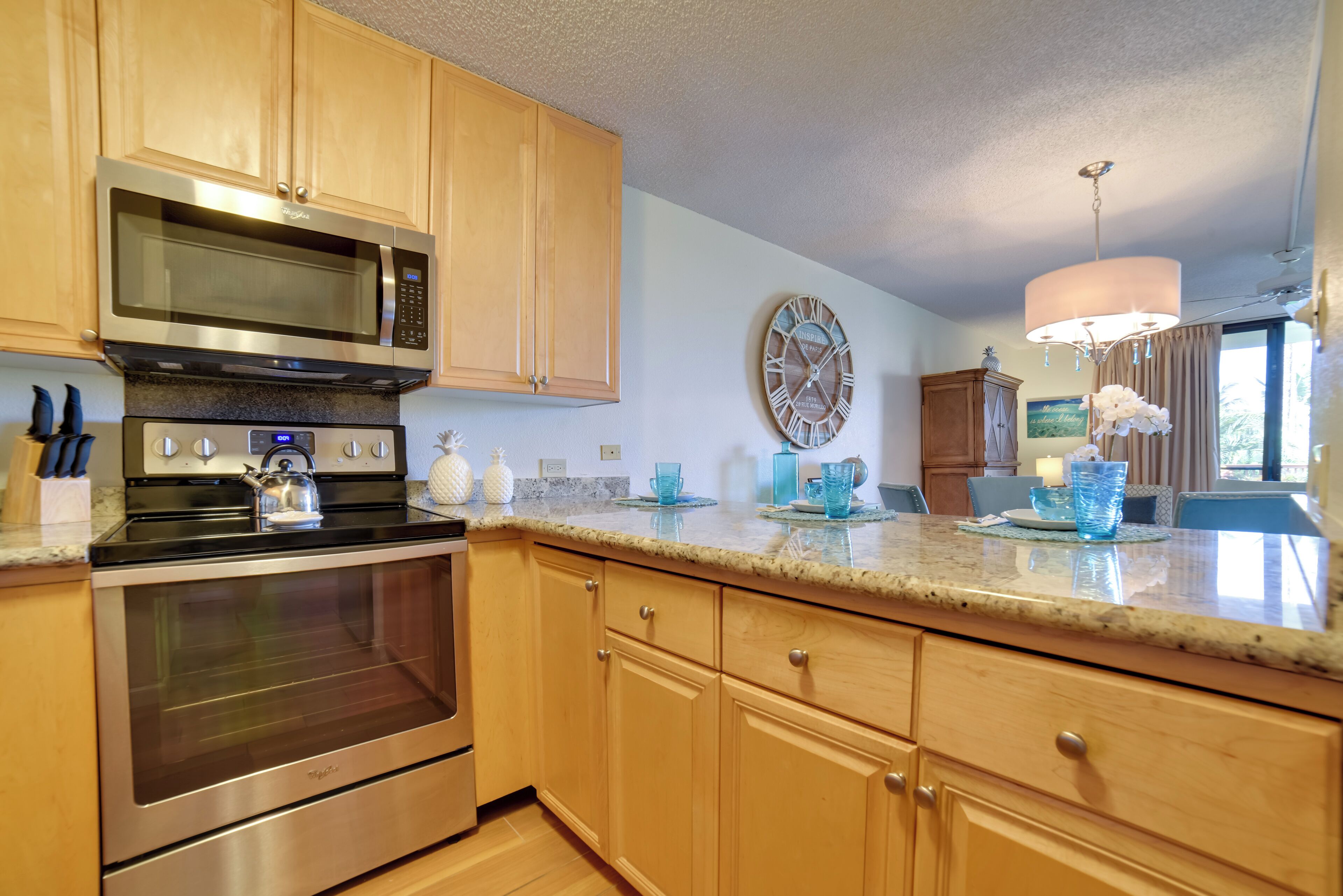 A kitchen with wooden cabinets, stainless steel appliances, a granite countertop, and a wall clock.
