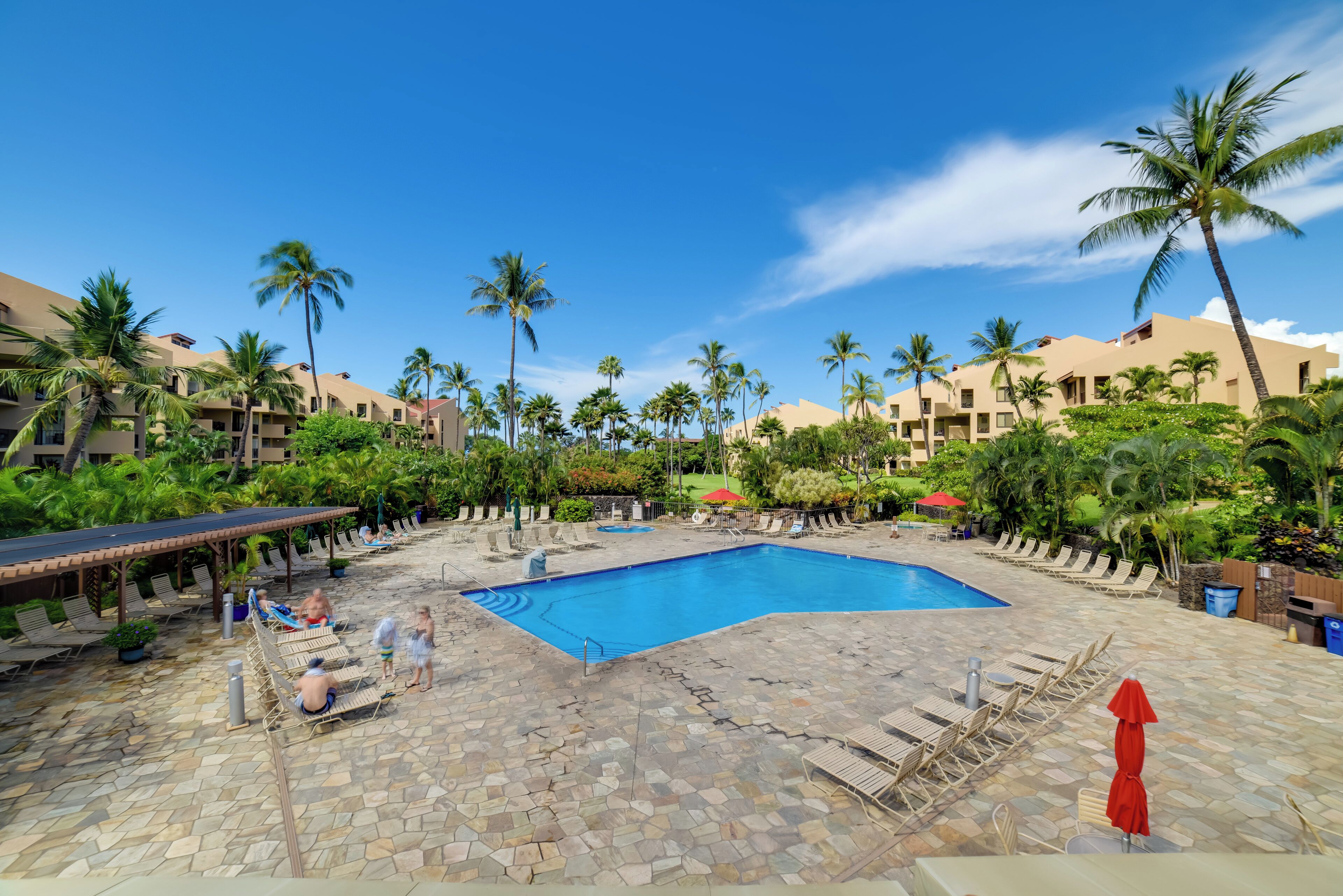 Ein Poolbereich eines Resorts mit großem Pool, Liegestühlen und Palmen.