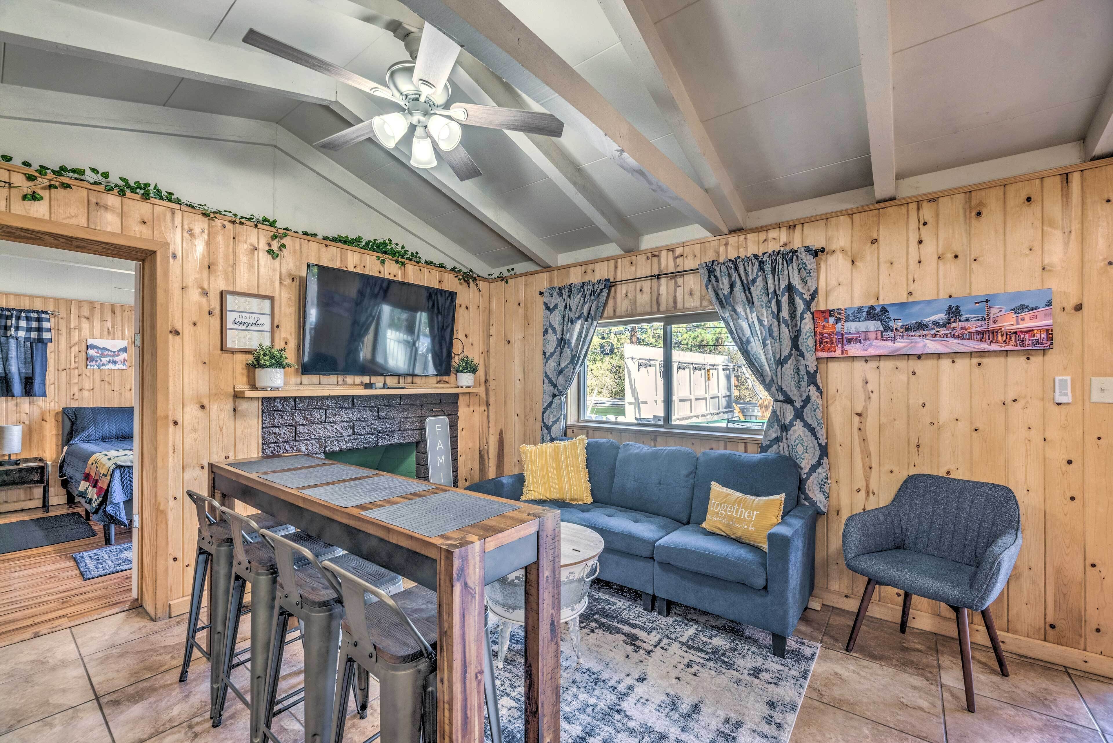 Une pièce chaleureuse au décor intérieur en bois, un coin repas avec des chaises en métal, un canapé bleu agrémenté de coussins et un téléviseur fixé au mur.