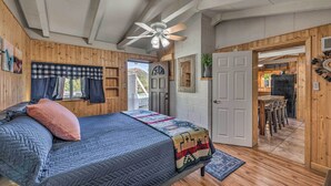 A wooden-paneled room with a bed, a ceiling fan, and a view of the outside. - Cabin w/ Mountain Views ~ 2 Mi to Ruidoso Midtown! (Ruidoso)