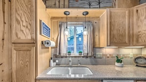 A kitchen with wooden cabinets, a granite countertop, a built-in dishwasher, and a window with curtains. - Cabin w/ Mountain Views ~ 2 Mi to Ruidoso Midtown! (Ruidoso)