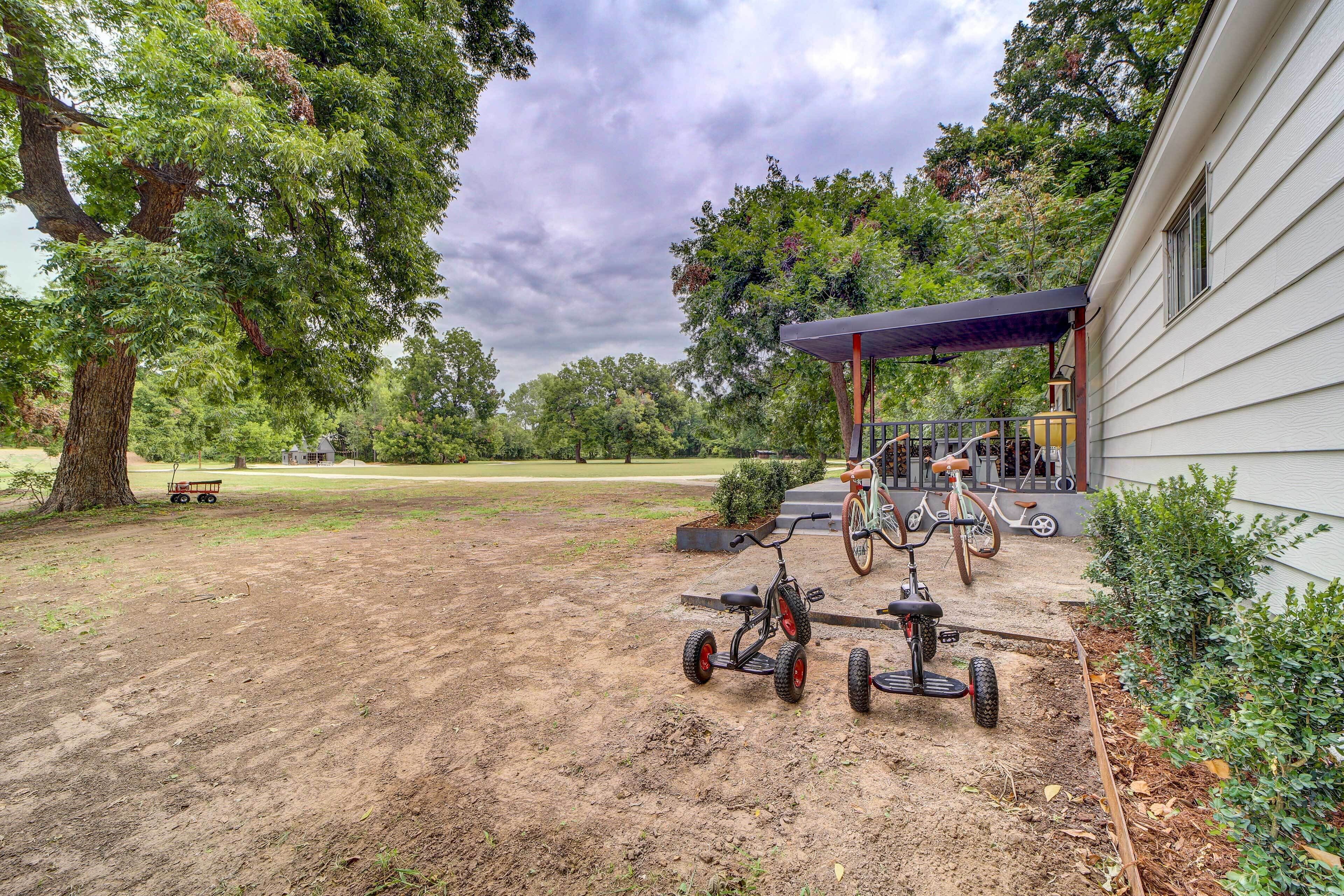 A backyard with a dirt path, a covered patio, and two tricycles.