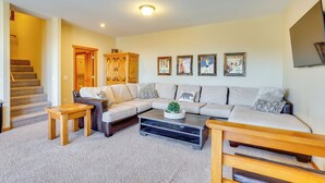 A living room with a sectional sofa, a coffee table, a small wooden table, and a staircase leading to another room. - Private Hot Tub: Scenic Granby Vacation Rental! (Granby)