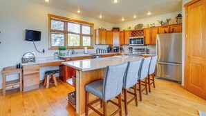 A modern kitchen with wooden cabinets, a stainless steel refrigerator, a large island with bar stools, and a window providing natural light. - Private Hot Tub: Scenic Granby Vacation Rental! (Granby)