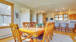 A dining area with a wooden table and chairs, a chandelier, and a view of the kitchen. - Private Hot Tub: Scenic Granby Vacation Rental! (Granby)