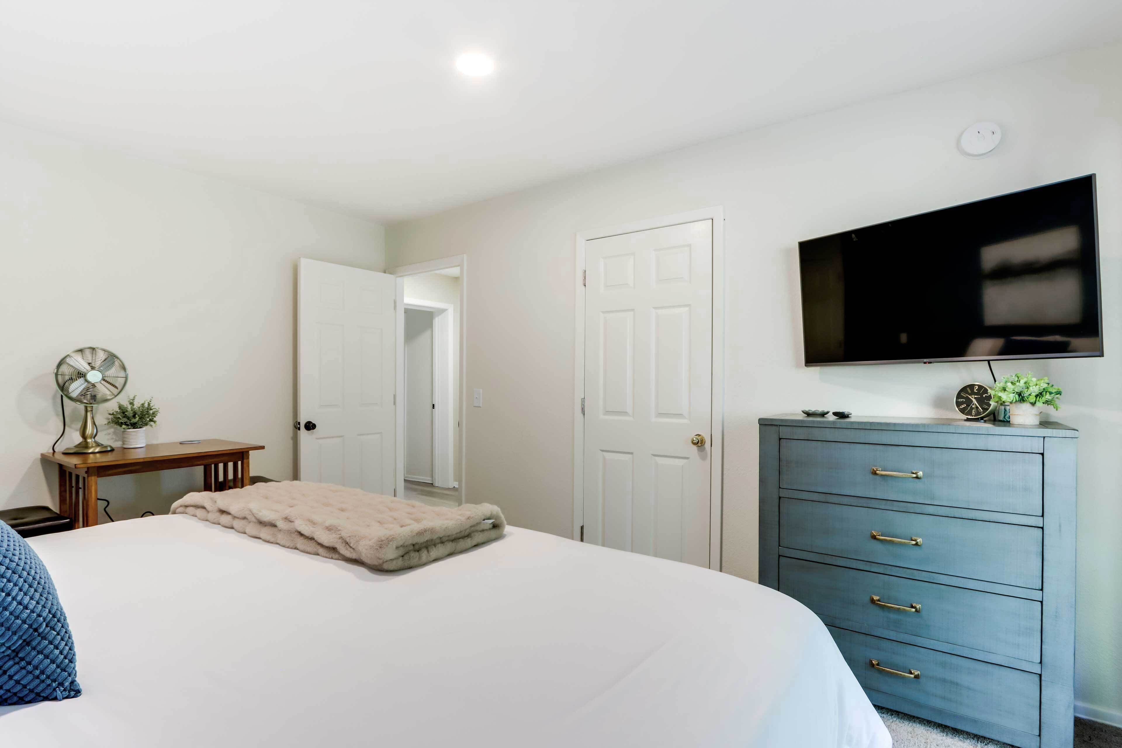 A bedroom with a bed, a dresser, a television mounted on the wall, and a door leading to another room.