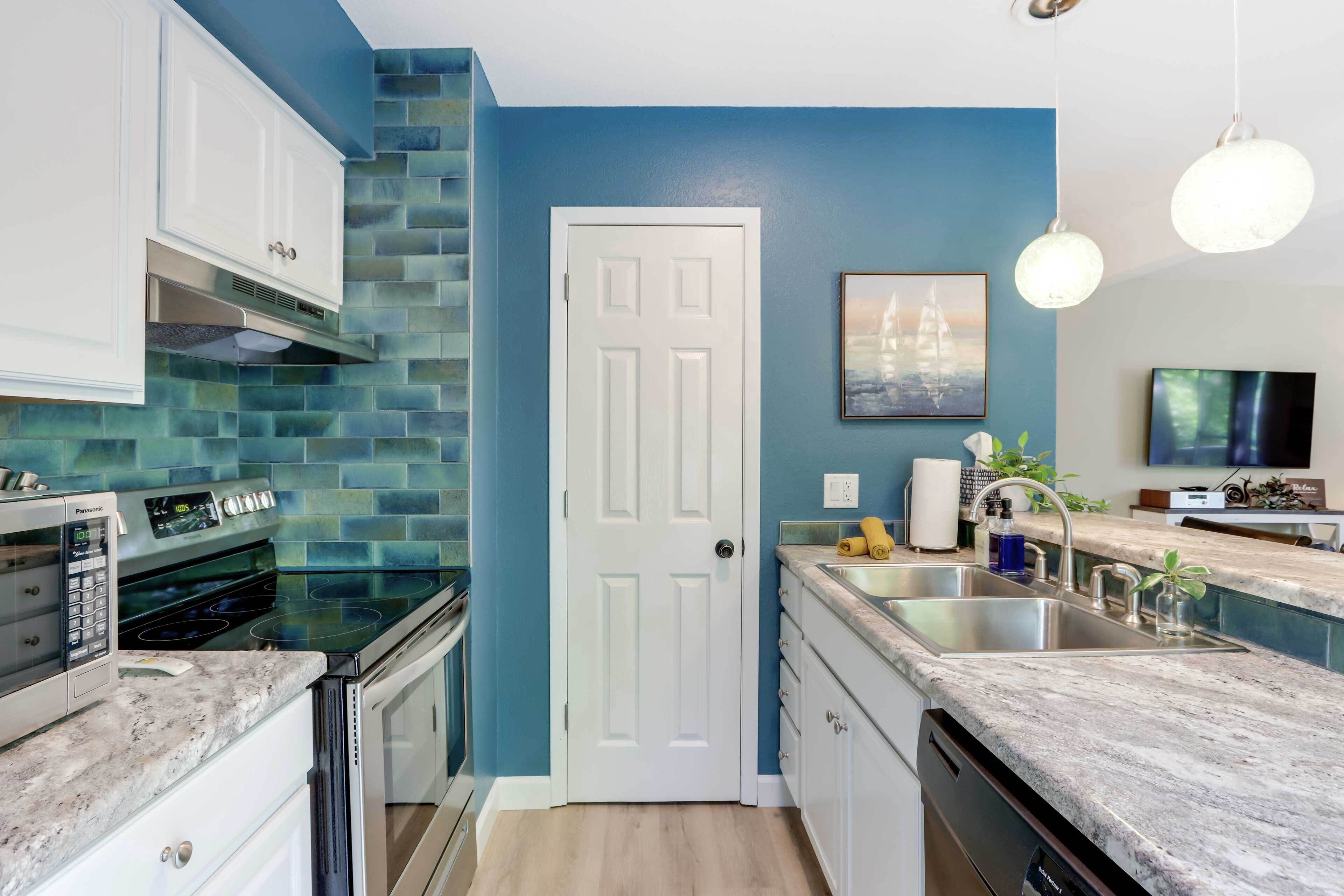 A modern kitchen with a blue backsplash, white cabinets, and stainless steel appliances.