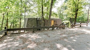 A rustic cabin with a wooden door and a brick exterior, surrounded by a wooden fence and trees. - Families w/ Pets! Lake-view Osage Beach Home (Osage Beach)