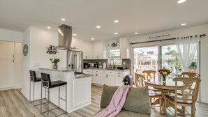 A modern kitchen with white cabinets, a central island, and a dining area with wooden chairs and a table. - 'breeze by the Marina' Chula Vista Getaway! (Chula Vista)