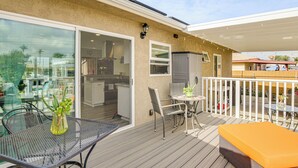 A covered outdoor patio with a table and chairs, a glass door leading to a kitchen, and a white fence. - 'breeze by the Marina' Chula Vista Getaway! (Chula Vista)