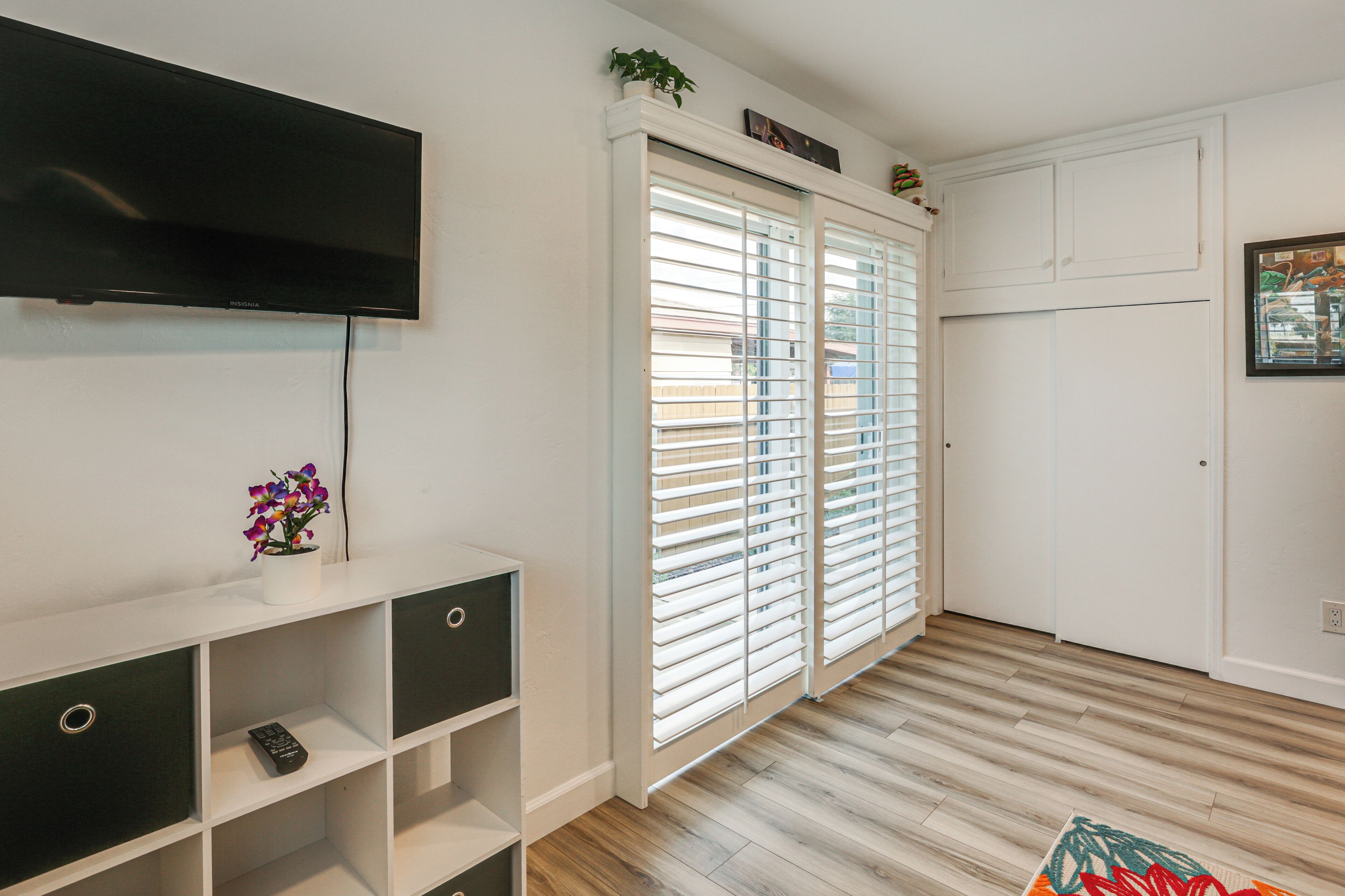 A modern living room with a flat-screen TV, a white entertainment unit, a sliding glass door, and a wooden floor.