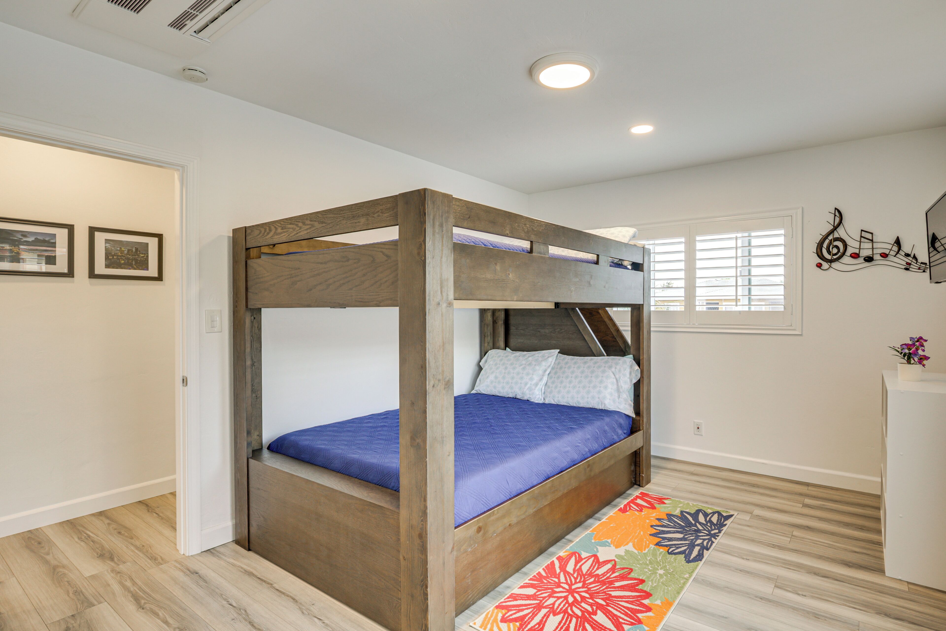 A bunk bed with a wooden frame and blue bedding, a colorful rug, and a wall with musical notes.