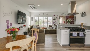 A modern kitchen with white cabinets, a stainless steel stove, and a dining area with a wooden table and chairs. - 'breeze by the Marina' Chula Vista Getaway! (Chula Vista)