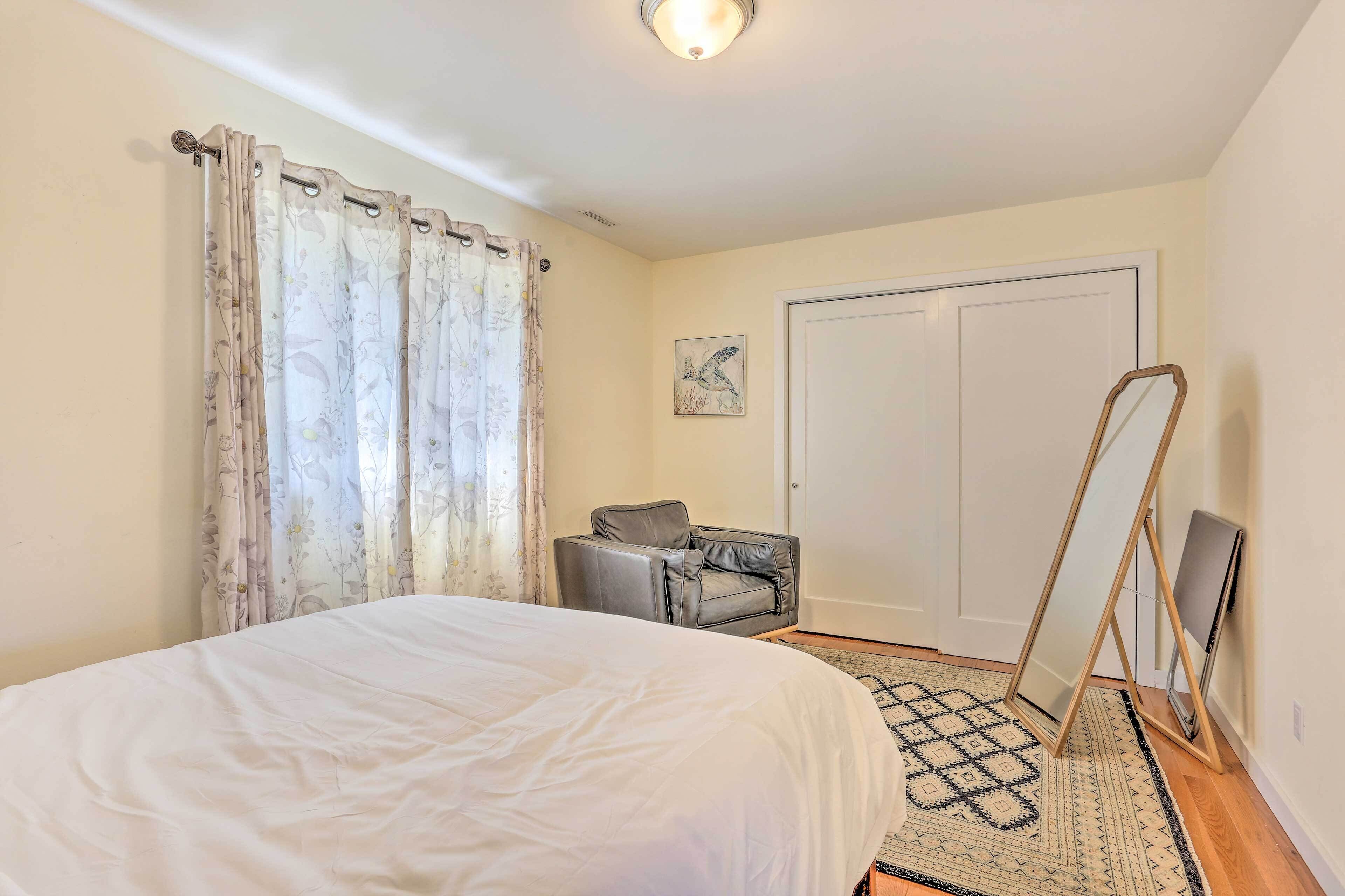 Un dormitorio con una cama, una silla gris, una puerta y un espejo de pie.