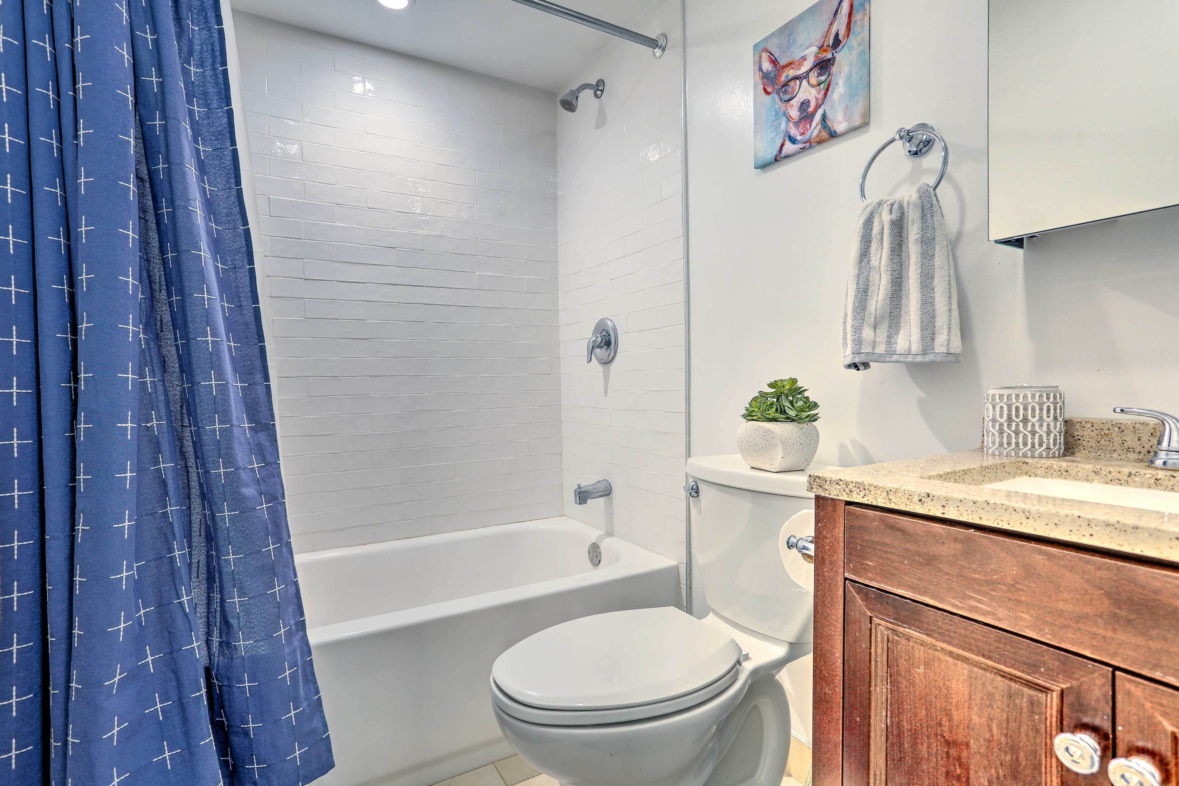 Une salle de bain avec une baignoire blanche, des toilettes, une douche avec une porte en verre, un lavabo avec un comptoir en granit et un meuble-lavabo en bois.