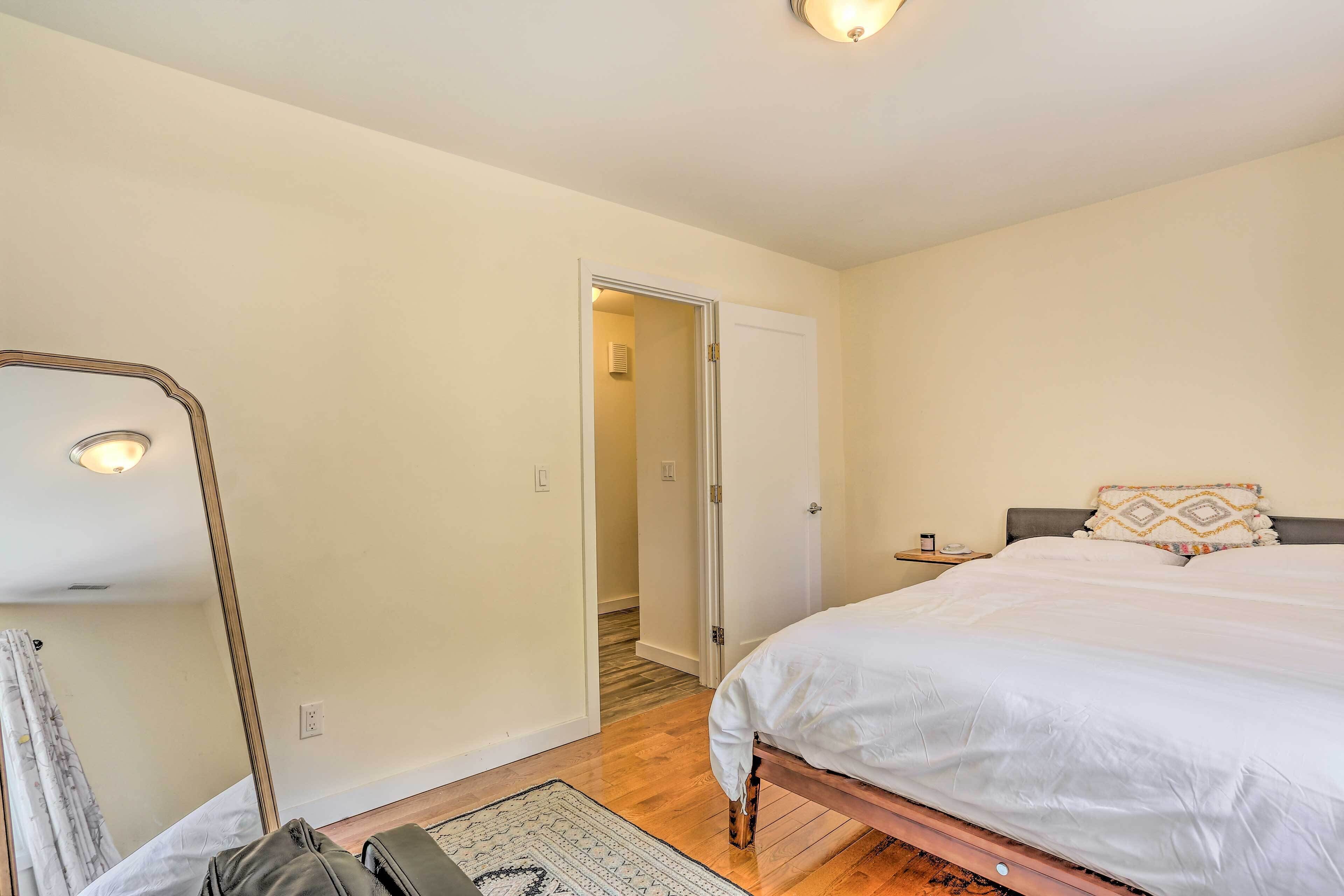 A bedroom with a bed, a nightstand, a mirror, and a door leading to another room.