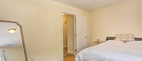 A bedroom with a bed, a nightstand, a mirror, and a door leading to another room.