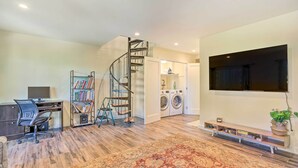 Un espacio habitable amplio con una escalera en espiral, un televisor de pantalla plana montado en la pared, una lavadora y una estantería.