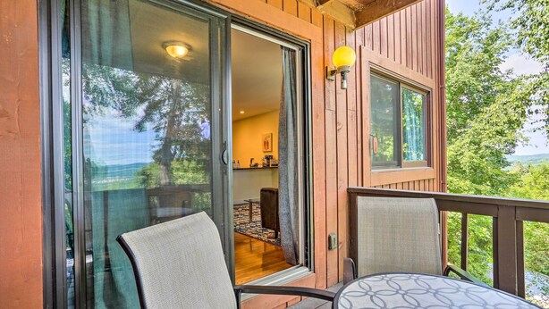 Una terraza de madera con un ventanal de vidrio que da a una habitación con cocina y comedor.