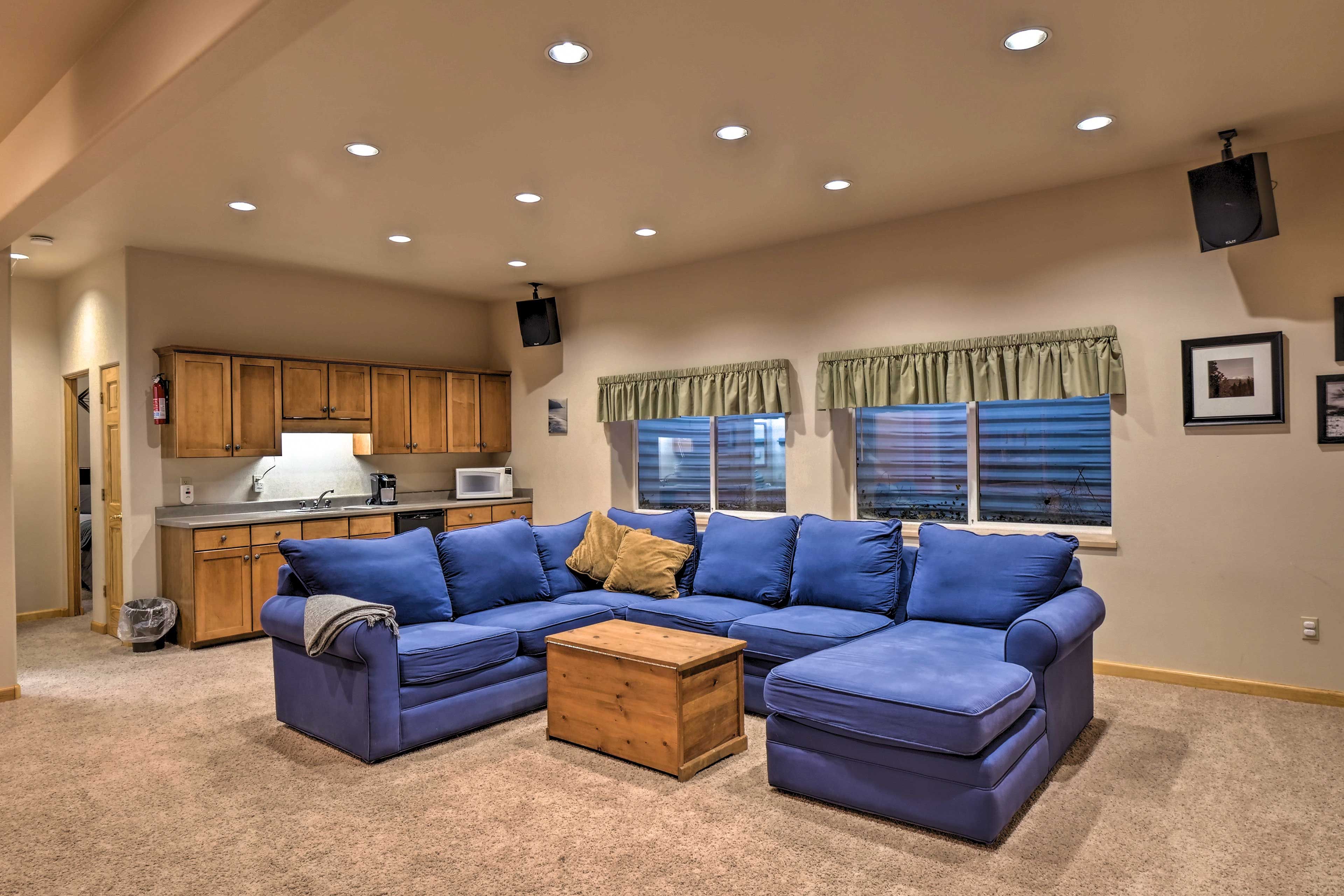 A living room with a sectional sofa, a wooden coffee table, and a kitchen in the background.