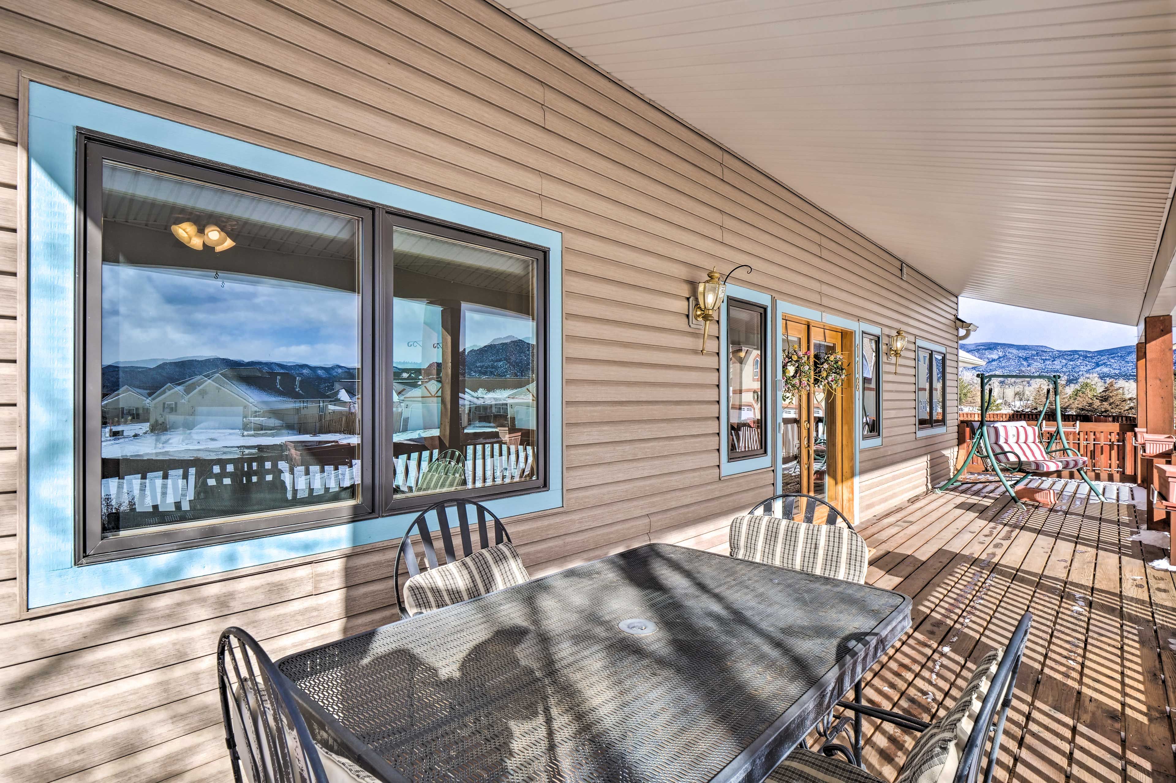 A covered outdoor patio with a table and chairs, large windows with a view of a snowy landscape, and a wooden deck.