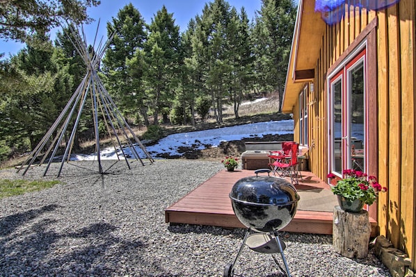 A wooden cabin with a deck, a teepee, and a barbecue grill.