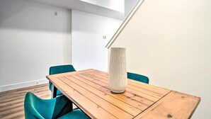 Et moderne værelse med et træbord og turkise stole, en høj vase og et ovenlysvindue.