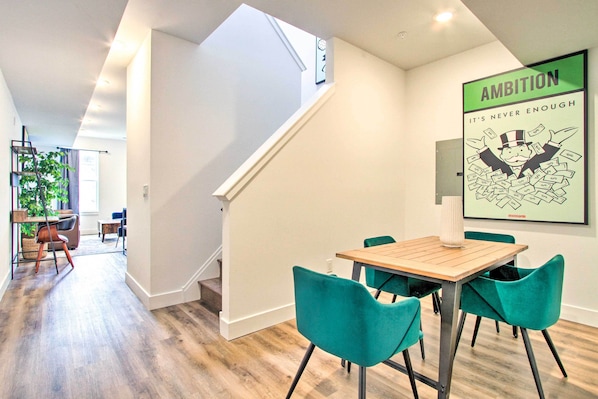 A modern interior with a dining area featuring a wooden table and teal chairs, a staircase, and a motivational poster on the wall.
