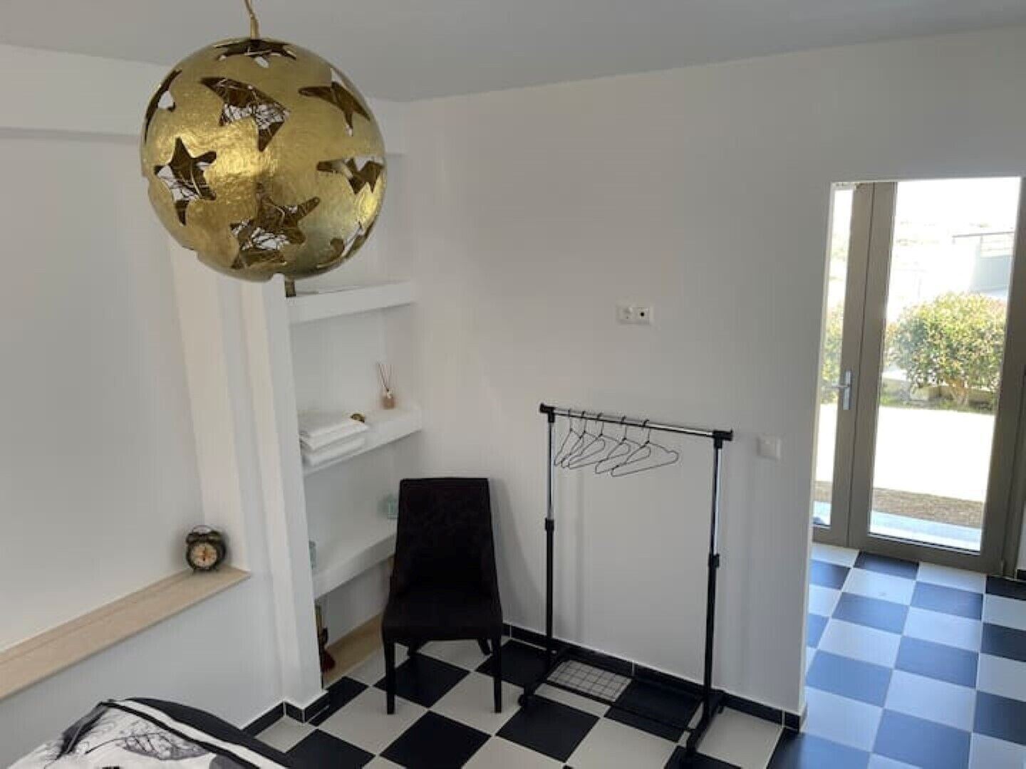 Ein Zimmer mit Schachbrettfußboden, einem schwarzen Stuhl, einem weißen Regal mit einer Uhr und einem Kleiderständer.